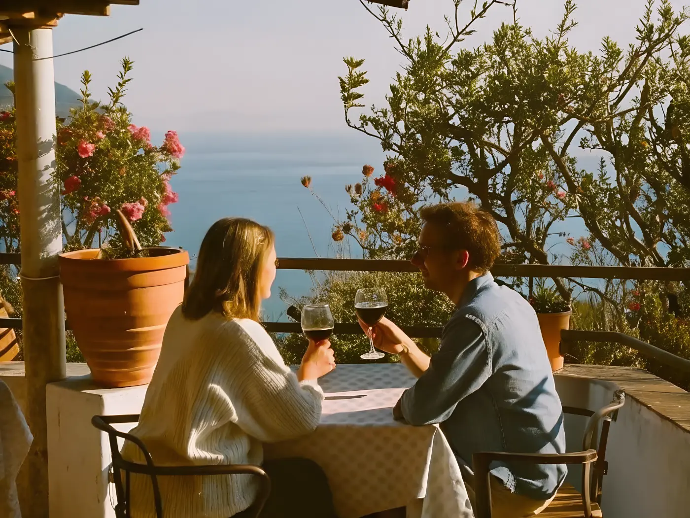 A couple toasting red wine on a sea-view terrace