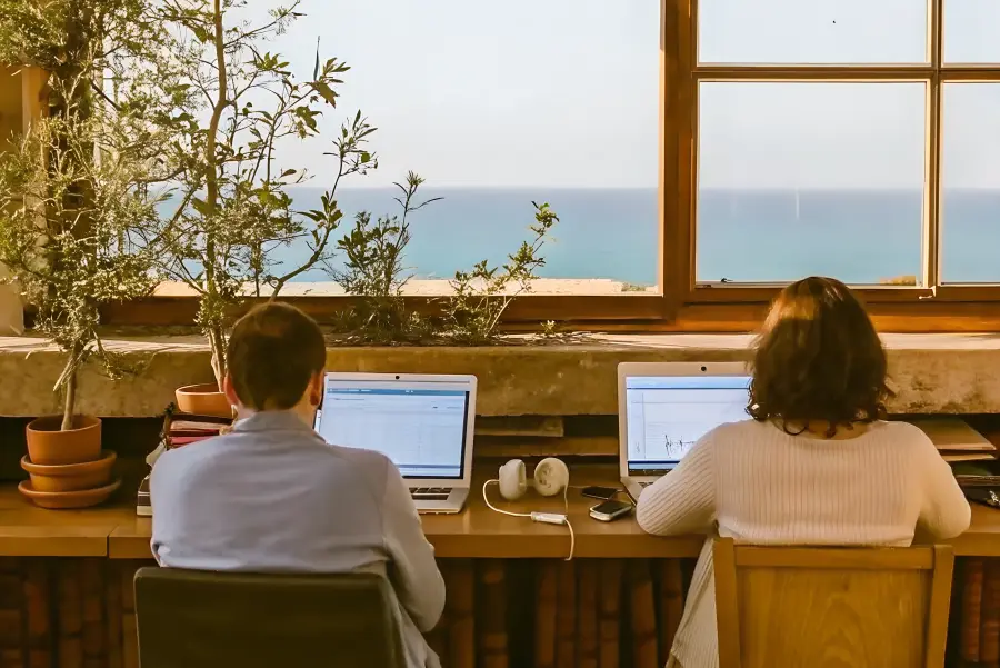 Two people working on laptops at a sea-view desk